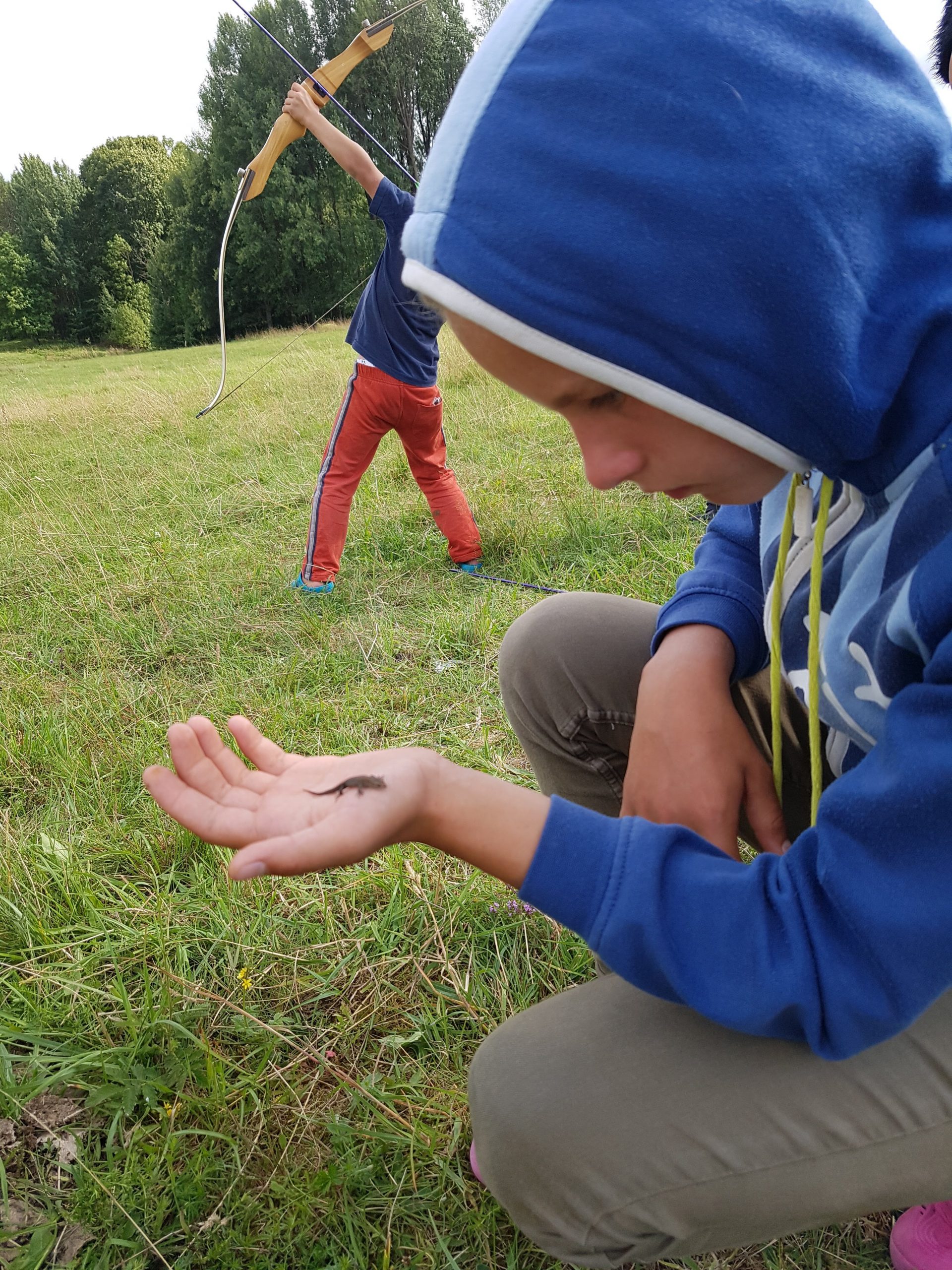Vaikas su driežu ant delno ir lankininkas fone